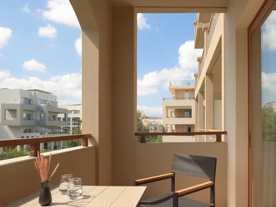 Balkon mit Tisch, Stuhl und Vasen, Blick auf moderne Hotelgebäude bei klarem Himmel.