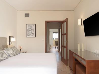 Hell eingerichtetes Hotelzimmer mit großem Bett, Fernseher an der Wand und Holzmöbeln.