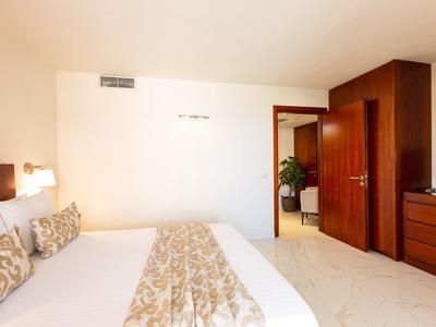 Habitación de hotel luminosa con cama doble, muebles de madera y acceso a un pasillo con plantas.