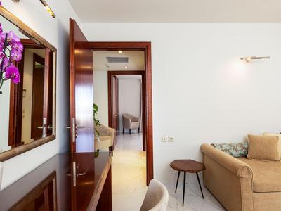 Vista a través de una puerta abierta hacia una habitación de hotel luminosa con sofá y mesa pequeña.