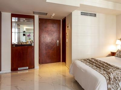 Habitación de hotel moderna con azulejos de mármol, muebles de madera marrón y cama grande con ropa blanca.