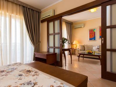 Una habitación de hotel luminosa con dormitorio y sala, muebles modernos y cortinas en la ventana.