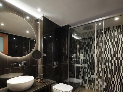 Baño moderno con espejo redondo iluminado, lavabo, inodoro y ducha con vidrio decorado.