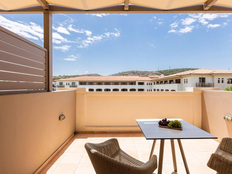 Balkon mit Stühlen, Tisch und Blick auf umliegende Gebäude und Hügel unter blauem Himmel.