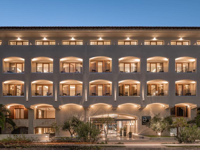 Beleuchtetes Hotelgebäude mit symmetrischen Balkonen und Eingang bei Abenddämmerung.