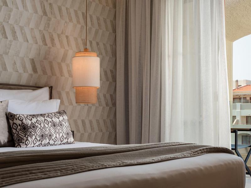 Gemütliches Hotelzimmer mit Bett, dekorativen Kissen und Blick auf Balkon und Gebäude.