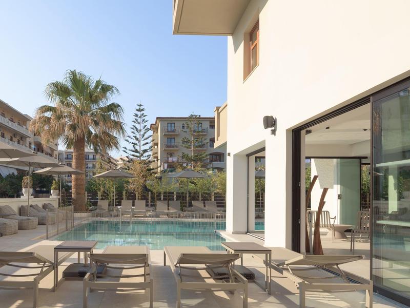 Moderner Hotelpoolbereich mit Liegestühlen und Palmen unter blauem Himmel.