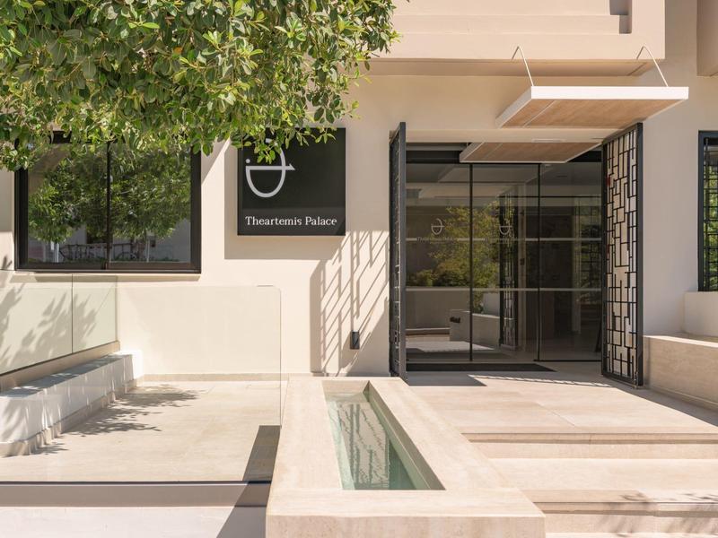 Moderner Hoteleingang mit Glas- und Metalltüren neben einem Baum und Außenbereich.