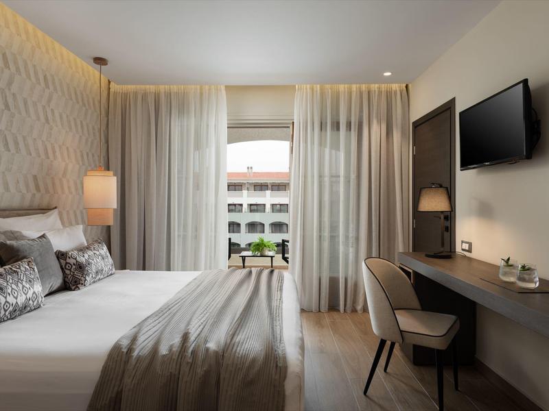 Modernes Hotelzimmer mit großem Bett, Schreibtisch, Fernseher und Blick auf einen Innenhof.