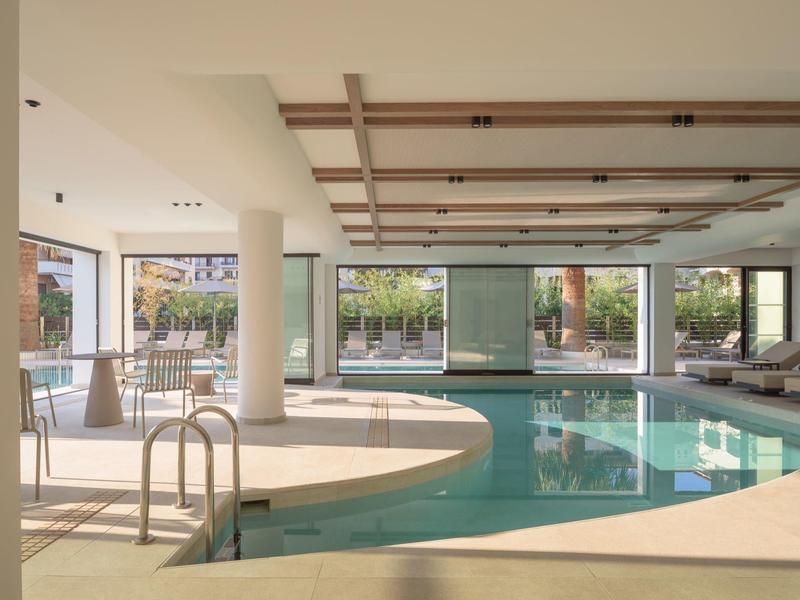 Innenpoolbereich mit großen Fenstern, Sitzgelegenheiten und Holzbalkendecke in einem Hotel.