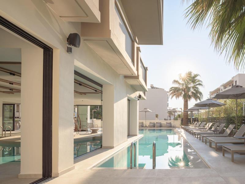 Moderner Hotelpool mit Liegestühlen und Palmen an einem sonnigen Tag.