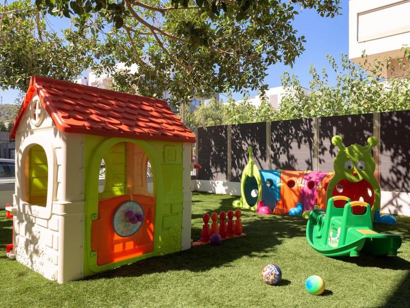 Bunter Kinderspielplatz mit kleinem Spielhaus, Rutsche und Bällen auf grünem Rasen.