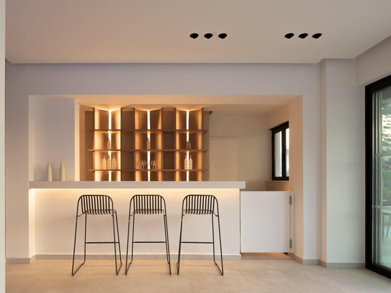 Moderner Hausbar-Bereich mit drei Metallhockern und warm beleuchteter Rückwand.