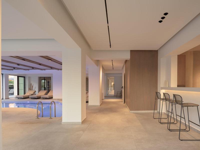 Moderner Hotelflur mit Barbereich, Stahlhockern und Blick auf Lounge mit Sofa und Kunstwerken.