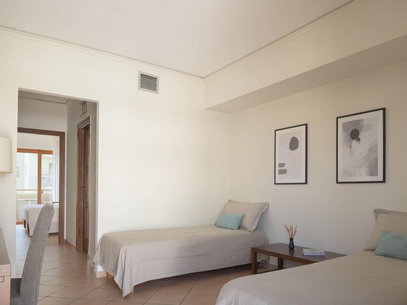 Ein helles Hotelzimmer mit zwei Einzelbetten, einfachen weißen Wänden und minimalistischer Dekoration.