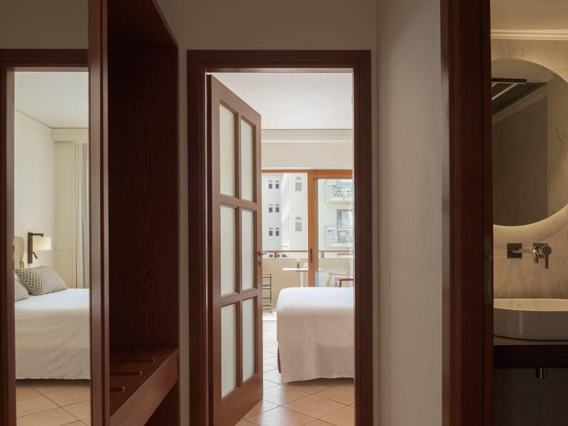 Blick durch einen Flur auf ein Schlafzimmer mit offenem Tür und angrenzendem Badezimmer mit rundem Spiegel.