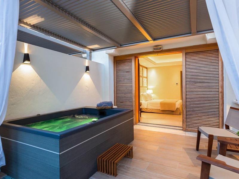 Moderner Whirlpool auf einer überdachten Terrasse eines Hotelzimmers mit Holzstühlen.