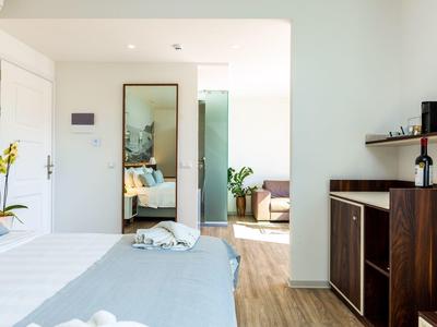 Hell eingerichtetes Hotelzimmer mit Bett, großem Spiegel und Holzmöbeln neben Holzboden.