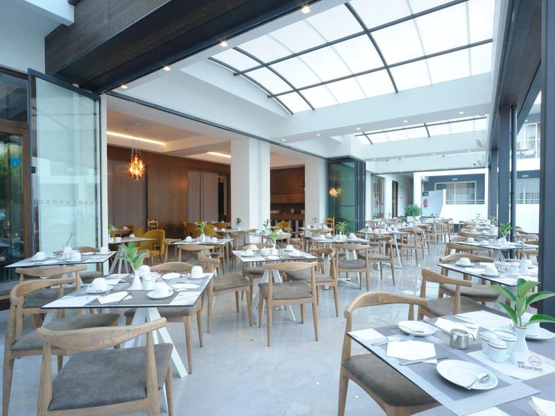 Modernes, helles Restaurant mit Glasdach, vielen Holztischen und Stühlen, klaren Linien und Pflanzen.