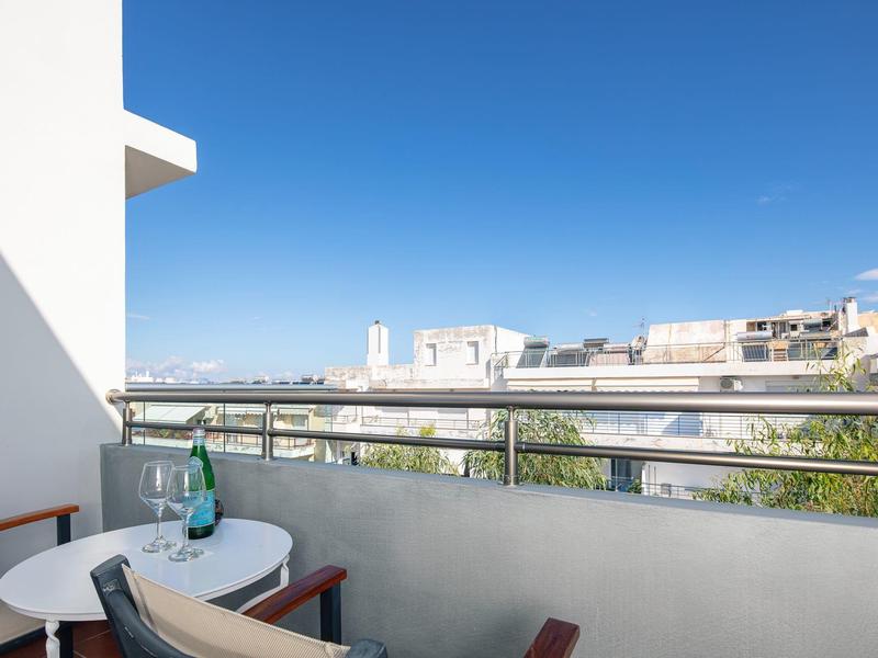 Balkon mit Tisch, Stühlen und blauer Wasserflasche, Blick auf Häuser und klaren Himmel.