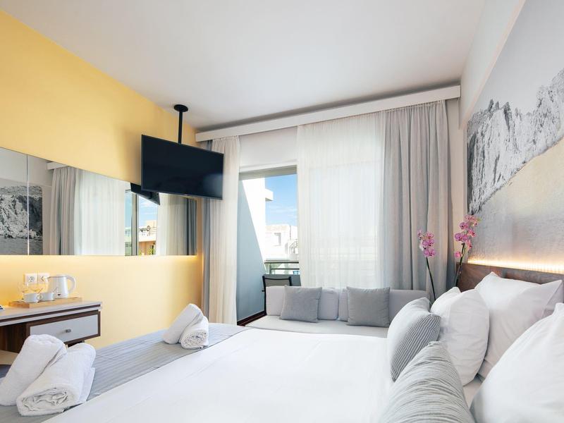 Modernes Schlafzimmer mit großem Bett, gelber Wand, TV an der Decke und Fenster mit Blick nach draußen.