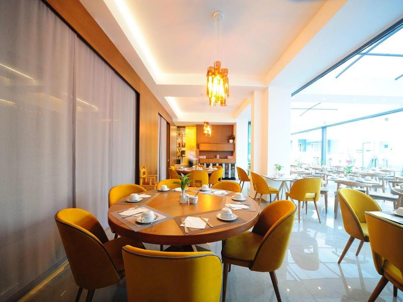 Moderner, hell beleuchteter Speisesaal mit gelben Stühlen und runden Tischen, große Fenster.