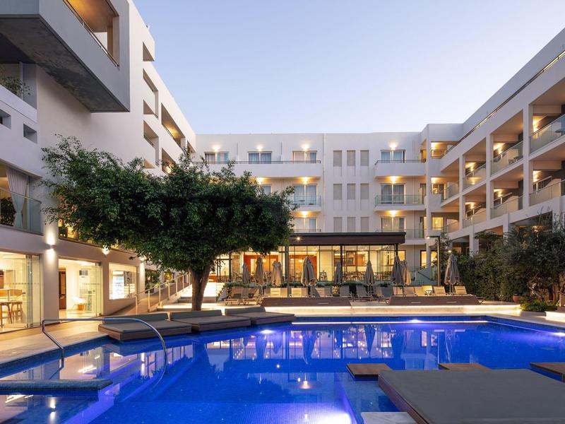 Moderner Wohnkomplex mit beleuchtetem Pool, Bäumen und dreistöckigen Gebäuden bei Abendlicht.