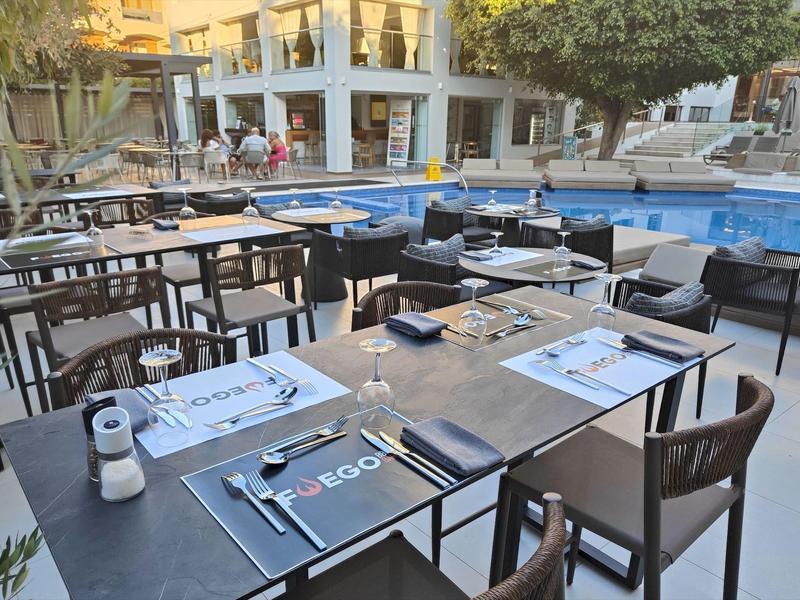 Outdoor-Restaurant mit schwarzen Tischen am Pool, weißen Menükarten und Holzstühlen bei Tageslicht.