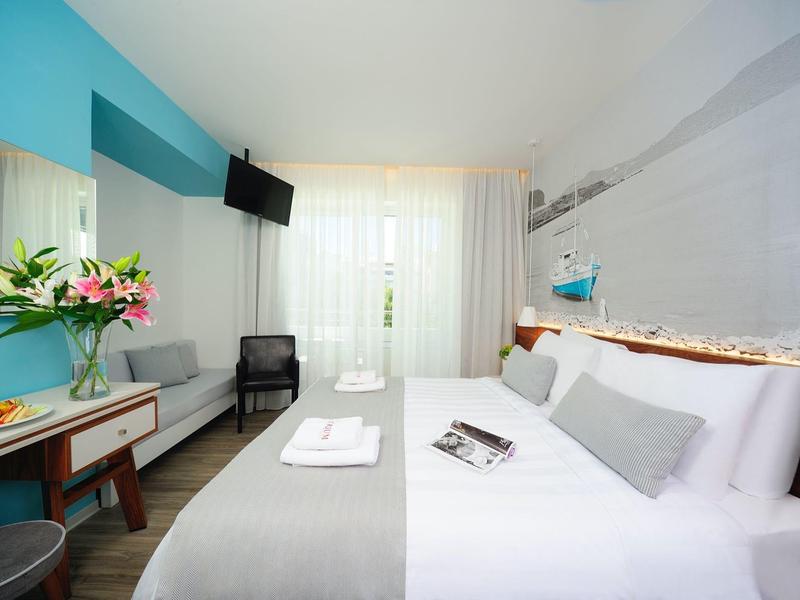 Helles, modernes Hotelzimmer mit Doppelbett, Fernseher, Schreibtisch und großer Fensterfront.