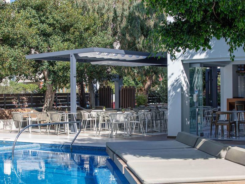 Moderner Poolbereich mit Liegen, Sitzgelegenheiten unter Pergola und viel Grün im Hintergrund.