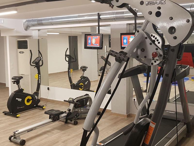 Kleines Fitnessstudio mit Rudergerät, Fahrrad-Ergometer und mehreren Geräten an der Wandspiegelwand.