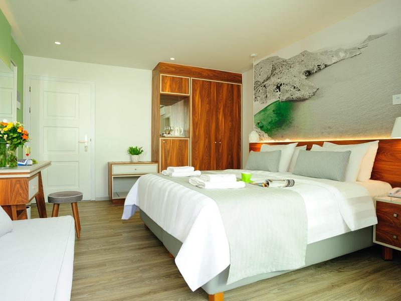 Helles Schlafzimmer mit Doppelbett, Holzmöbeln, großem Wandbild und Blumen auf dem Tisch.