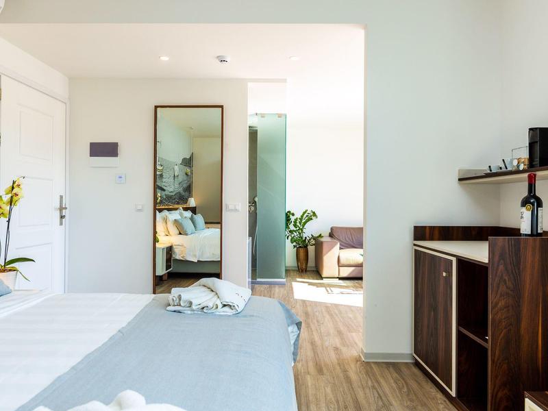 Hell eingerichtetes Hotelzimmer mit Bett, großem Spiegel und Holzmöbeln neben Holzboden.