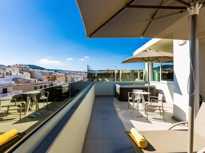 Moderner Balkon mit Sonnenschirmen, Stühlen und Tischen, Blick auf Stadt und Berge.