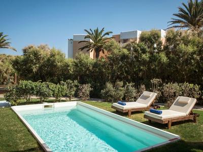 Ein rechteckiger Pool im Garten mit zwei Liegestühlen, grünen Büschen und Palmen im Hintergrund.