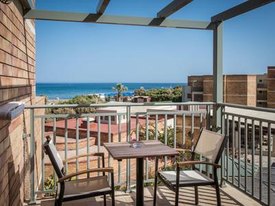 Balkon mit Tisch und zwei Stühlen, Blick auf Gebäude und blauen Himmel am Meer.