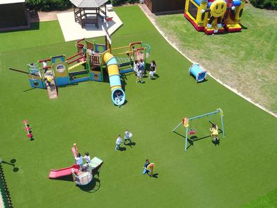 Großer Spielplatz mit grüner Spielfläche, Schaukeln, Rutschen und Klettergerüsten aus buntem Material.