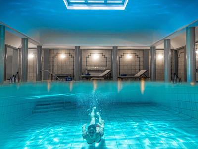 Helles Hallenbad mit Schwimmer, hellblauen Wasser und großem Dachfenster.