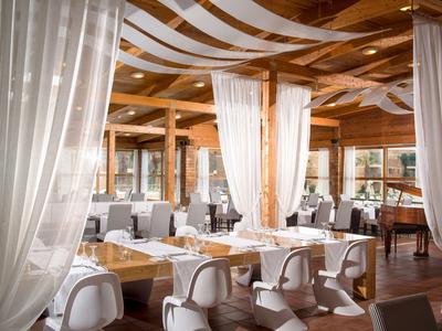Helles Restaurant mit Holzbalken, weißen Vorhängen und gedeckten Tischen in modernem Stil.