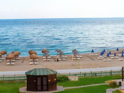 Strand mit Liegestühlen, Sonnenschirmen, Sand und ruhigem Meer im Hintergrund.