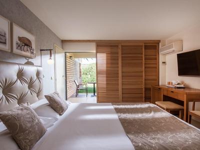 Helles Schlafzimmer mit großem Bett, Kopfteil, Kleiderschrank, Schreibtisch und Fernseher an der Wand.