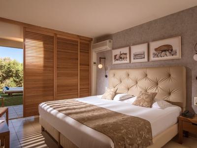 Helles Schlafzimmer mit großem Bett, Holzmöbeln, Kunst an der Wand und Blick auf Balkon mit Aussicht.