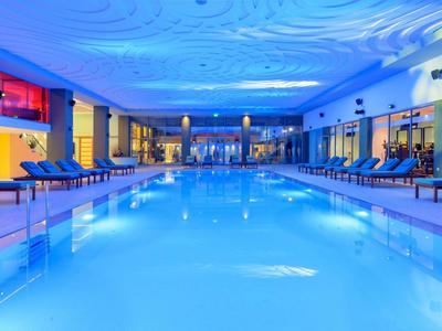 Großes Hallenbad mit blauer Beleuchtung, Liegestühlen und moderner, heller Inneneinrichtung.