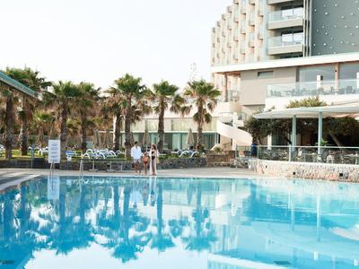 Piscina dell'hotel con lettini, palme e edificio moderno sullo sfondo.