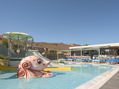 Piscina esterna con scivoli d'acqua e piscina per bambini in un hotel sotto un cielo azzurro.
