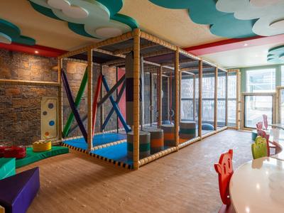 Area giochi interna luminosa e moderna con struttura per arrampicata e mobili colorati in un hotel.