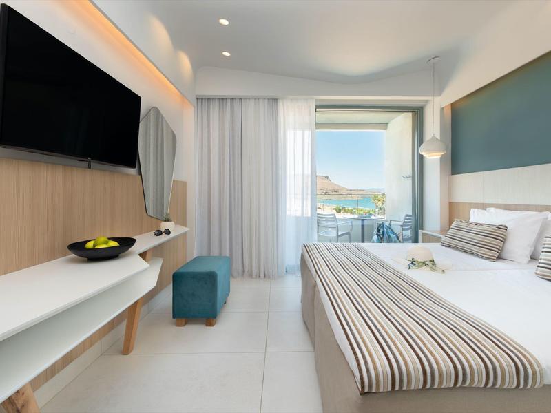 Moderní hotelový pokoj s manželskou postelí, TV na stěně, balkonem a výhledem na moře.
