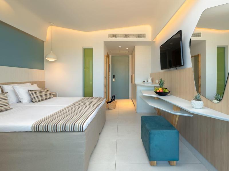 Moderní hotelový pokoj s manželskou postelí, velkým zrcadlem a minimalistickým zařízením.