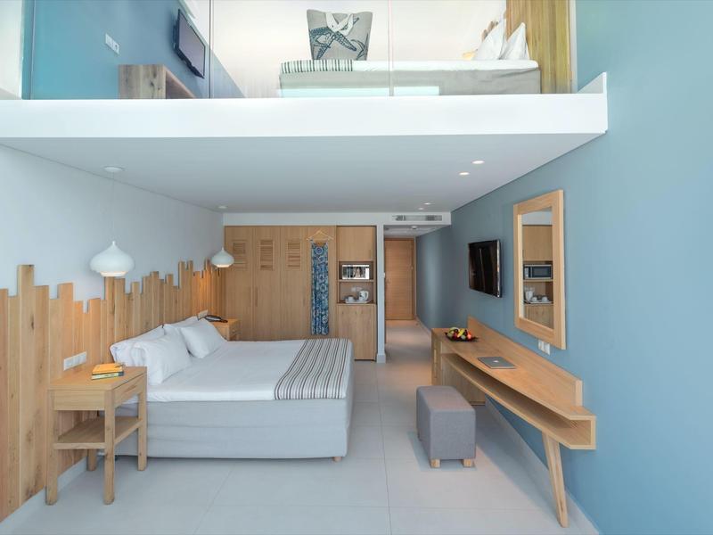 Moderní hotelový pokoj s manželskou postelí, světlým dřevěným stolem a modrými stěnami.