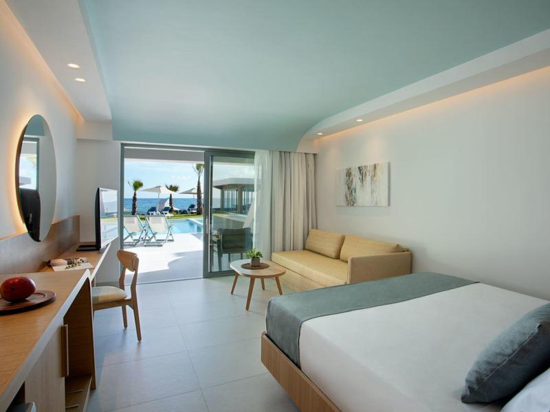 Moderní hotelový pokoj s manželskou postelí, pohovkou, psacím stolem a výhledem na venkovní bazén.